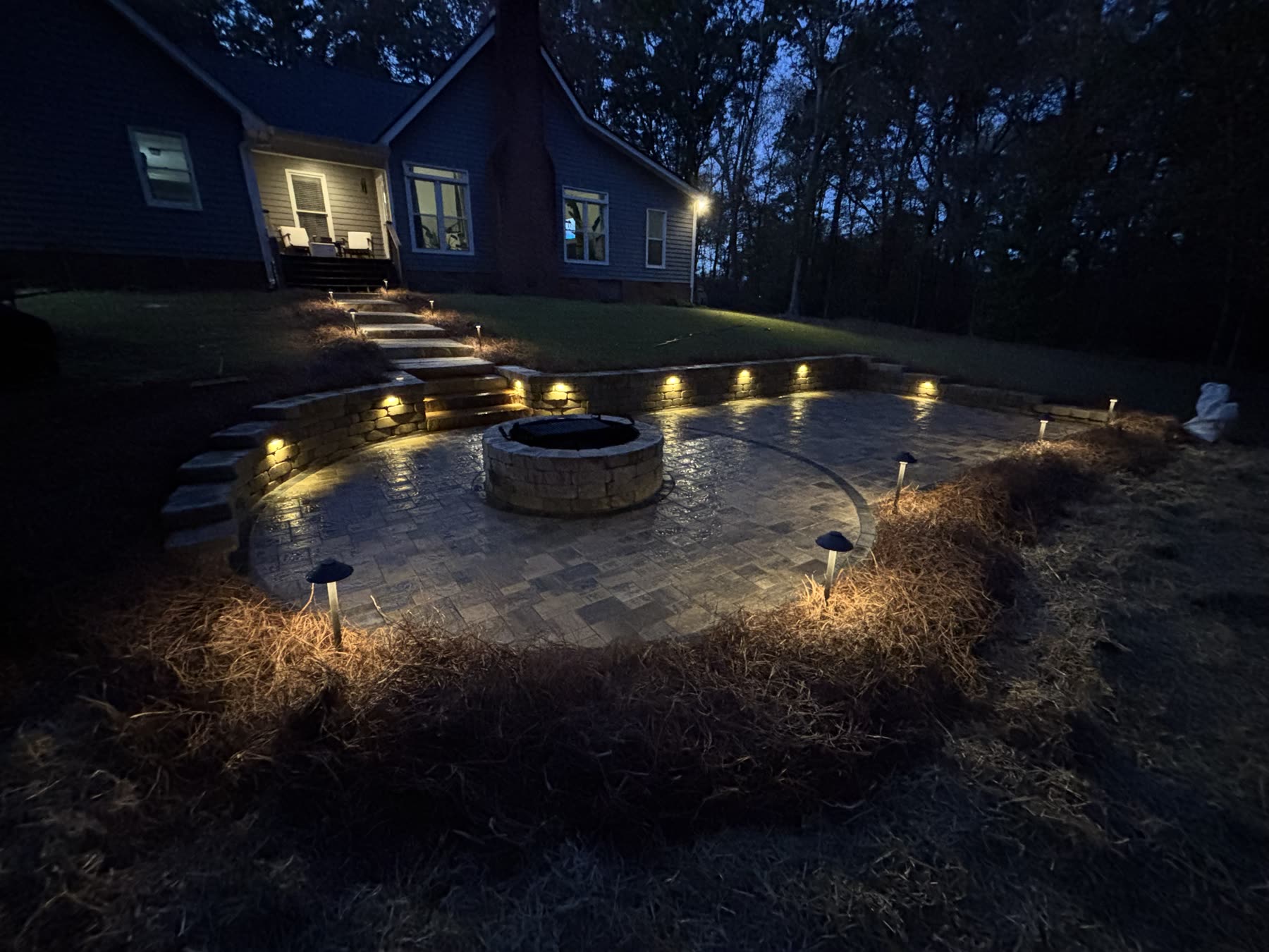 Fire pit patio with retaining wall and hardscape lighting at night North Georgia — built by Kaizen Scapes